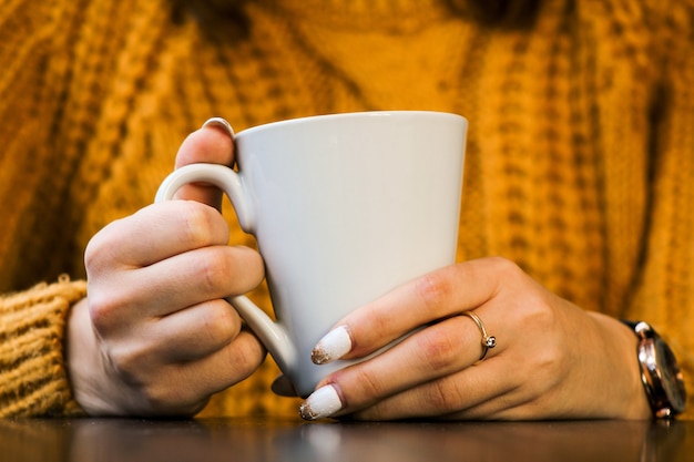 closeup de mãos femininas com uma caneca de bebida. Mulher bonita em suéter amarelo segurando uma xícara de chá