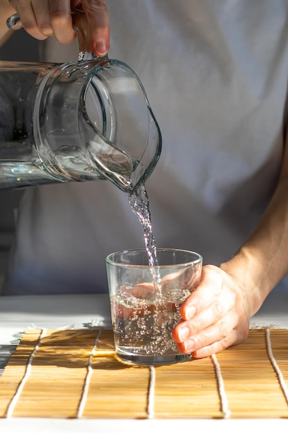 Closeup de mãos femininas derramando água potável em um copo de rituais matinais para a saúde
