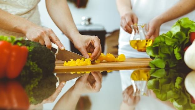 Closeup de mãos humanas cozinhando na cozinha. Mãe e filha ou duas amigas cortando legumes para salada fresca. Conceitos de amizade, jantar em família e estilo de vida.