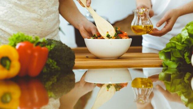 Closeup de mãos humanas cozinhando na cozinha Mãe e filha ou duas amigas cortando legumes para salada fresca Jantar em família de amizade e conceitos de estilo de vida