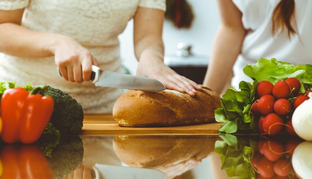 Closeup de mãos humanas cozinhando na cozinha. Mãe e filha ou duas amigas cortando pão para o jantar. Conceitos de amizade, família e estilo de vida.