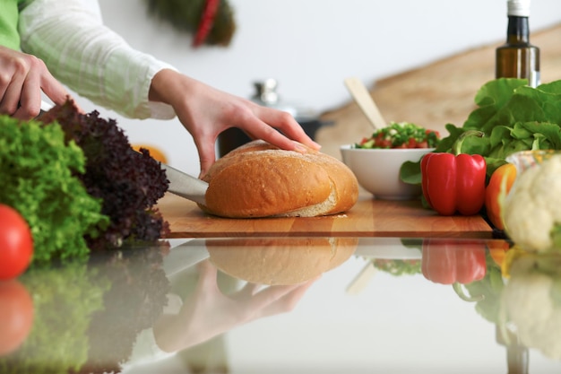 Closeup de mãos humanas cozinhando na cozinha na mesa de vidro com reflexão. Dona de casa cortando pão.