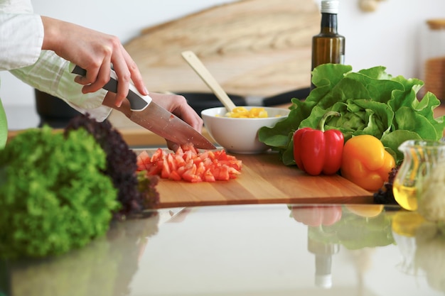 Closeup de mãos humanas cozinhar salada de legumes na cozinha na mesa de vidro com reflexão. refeição saudável e conceito vegetariano