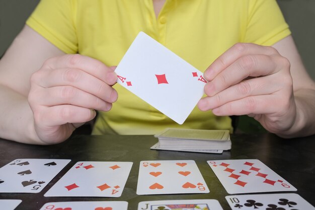 Foto closeup de mãos segurando um ás de ouros. a mulher na mesa está jogando paciência. jogos de tabuleiro e cartas, atividades de lazer em casa.