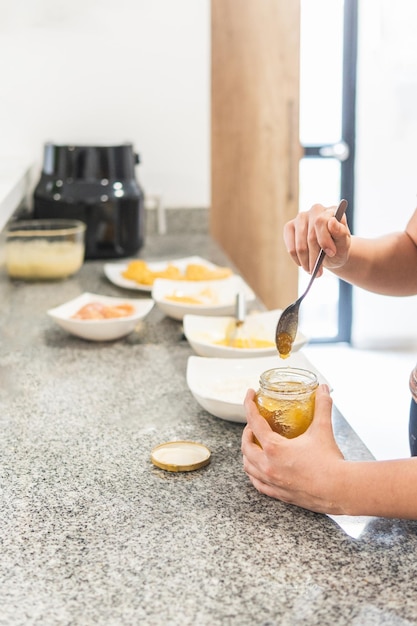 Closeup de mãos tirando mel de um recipiente ao lado de outros ingredientes no balcão da cozinha