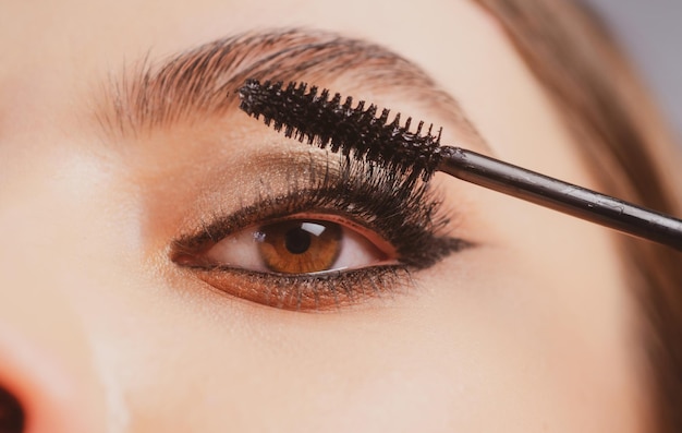 Closeup de maquiagem dos olhos aplicando máscara em exuberantes jovem se maquiando com o rosto de olhos de pincel