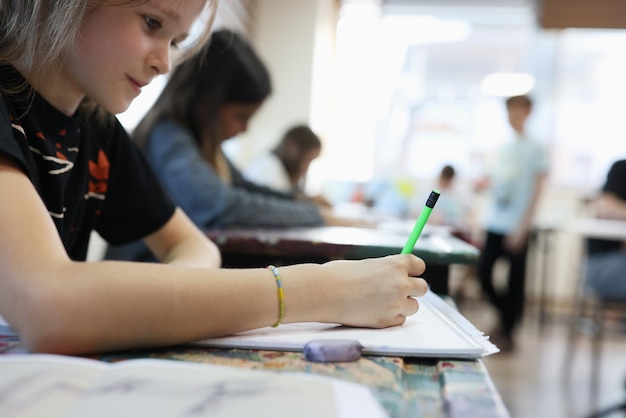 Closeup de menina sorridente sentada na mesa da escola e escrevendo desenho de aluno na arte de educação do álbum