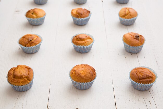 Closeup de muffins de baunilha caseiros em copos de papel azul em fileiras sobre fundo branco de madeira