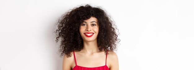 Foto closeup de mulher bonita com penteado encaracolado usando vestido vermelho e batom sorrindo feliz em veio