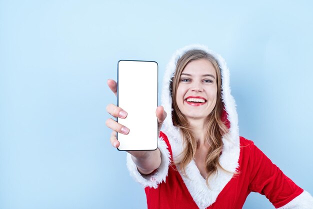 Closeup de mulher caucasiana feliz vestindo roupas de papai noel apontando para o smartphone