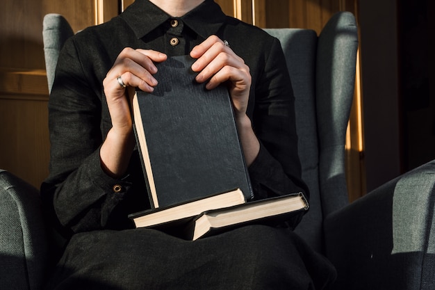 Closeup de mulher de vestido preto, segurando as mãos segurando livros no colo