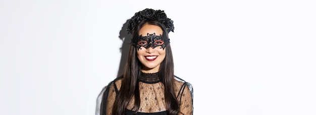 Closeup de mulher misteriosa em grinalda gótica e máscara preta sorrindo para a câmera celebrando o halloween