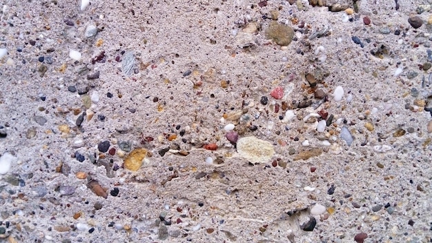 Closeup de pavimento de concreto com elementos embutidos as pedras se destacam em diferentes tamanhos e cores superfície áspera não uniforme de um produto de concreto seixos pequenos amarelos rosa brancos pretos