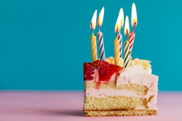 Closeup de pedaço de bolo de aniversário bonito saboroso apetitoso com muitas velas. Conceito de feriado de aniversário.