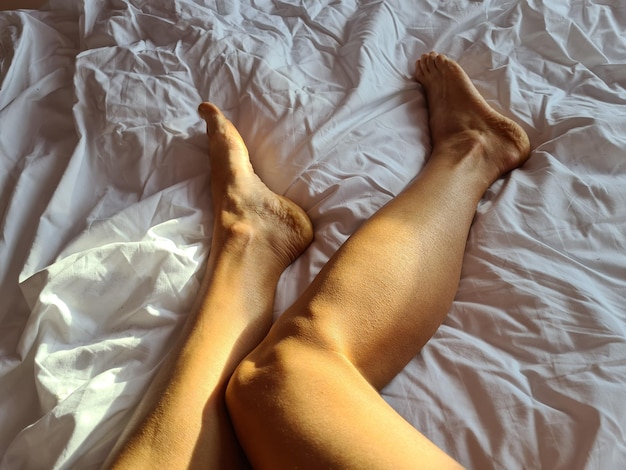 Closeup de pernas de mulher sob o cobertor branco na cama