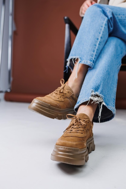 Closeup de pernas femininas em jeans azul e tênis de camurça marrom tênis casuais de couro feminino