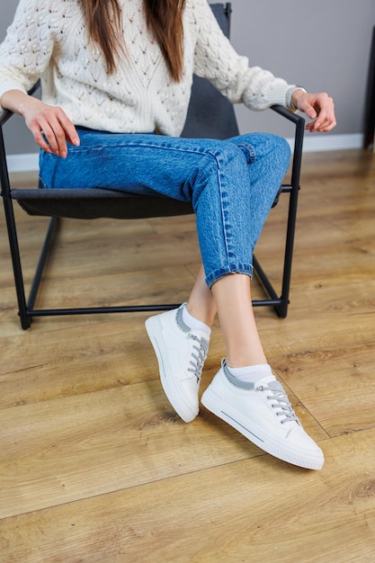 Closeup de pernas femininas em jeans e tênis brancos casuais Sapatos casuais confortáveis para mulheres Tênis femininos de couro branco