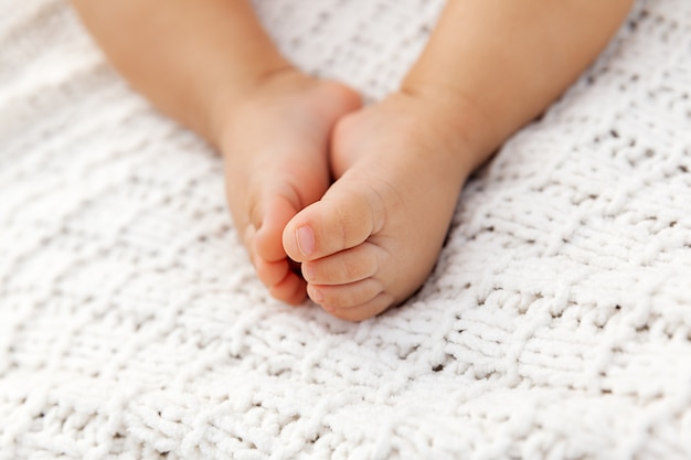 Foto closeup de pés de bebê adorável no cobertor de malha como pano de fundo em um foco seletivo, pernas infantis à luz natural