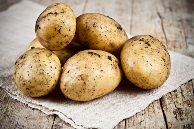 Closeup de pilha de batatas sujas orgânicas frescas na toalha de linho em madeira rústica