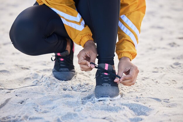 Closeup de praia e sapatos de gravata de mulher para uma corrida ao ar livre para fitness, saúde e bem-estar à beira-mar Atleta de esportes e zoom de corredora amarrando cadarços para um treino cardiovascular ou exercício à beira-mar