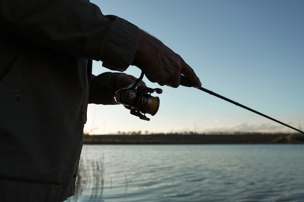 Closeup de roda de vara de pesca, homem pescando com um belo pôr do sol.