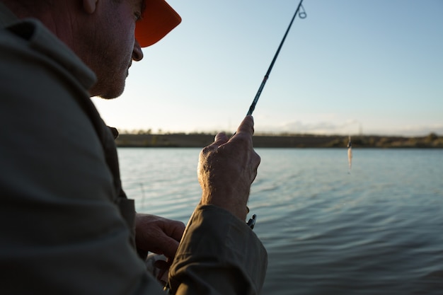 Closeup de roda de vara de pesca, homem pescando com um belo pôr do sol.