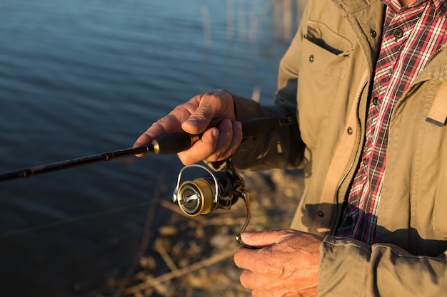 Foto closeup de roda de vara de pesca, homem pescando com um belo pôr do sol.