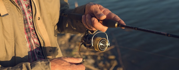 Closeup de roda de vara de pesca, homem pescando com um belo pôr do sol.