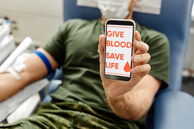 Closeup de soldado doando sangue e segurando smartphone para câmera com dar sangue salvar vida no scre