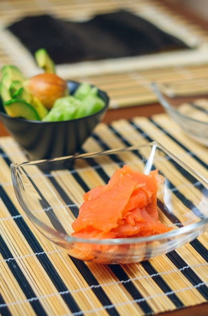 Closeup de tigelas com salmão, abacate e pepino cortado pronto para preparar sushi