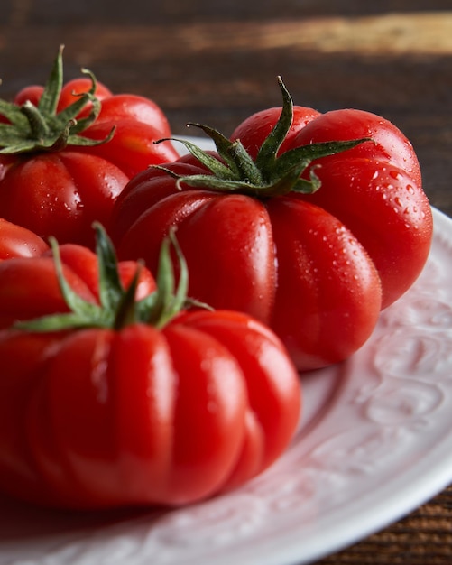 Closeup de tomates vermelhos frescos raf na chapa branca sobre fundo de madeira Conceito de comida