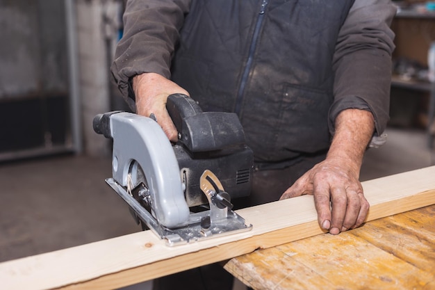 Closeup de um carpinteiro usando uma serra circular para cortar uma grande prancha de madeira