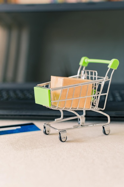 Closeup de um carrinho de compras com uma caixa ao lado de um laptop e cartão de crédito na mesa