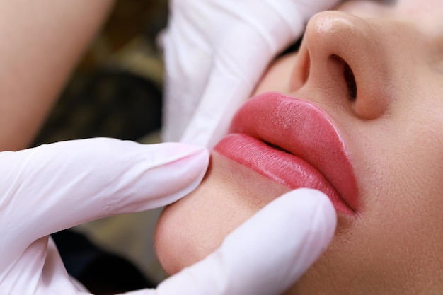 Foto closeup de um mestre de maquiagem permanente segurando os lábios de um modelo mostrando o trabalho concluído de maquiagem permanente dos lábios