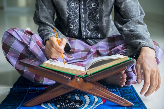 Closeup de um muçulmano devoto lendo o Alcorão no suporte de madeira durante o Ramadã em casa