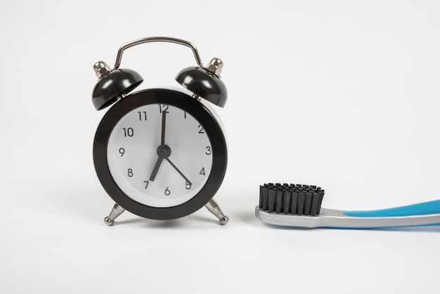 Closeup de um pequeno despertador preto e uma escova de dentes em um fundo branco