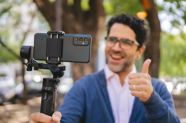 Closeup de um telefone inteligente em um gimbal sendo usado por um homem de meia-idade embaçado com o polegar para cima