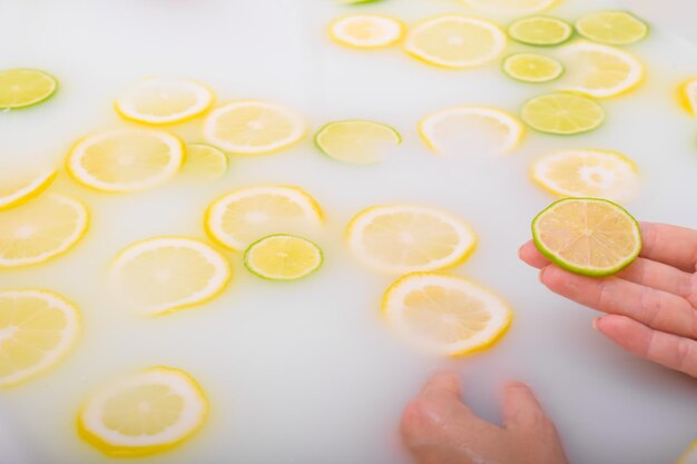 Closeup de uma mão feminina segurando uma fatia de frutas cítricas em um banho de leite