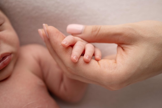 Closeup de uma mão pequena de um bebê com dedos minúsculos e braço da mãe em um fundo branco Bebê recém-nascido segurando o dedo dos pais após o nascimento O vínculo entre mãe e filho Conceito de família feliz