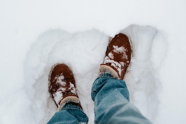 Closeup do homem vestindo jeans azul e botas marrons de inverno em pé no monte de neve ao ar livre vista superior
