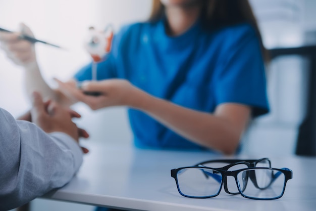 Closeup de una doctora asiática hablando con un paciente anciano mostrando el modelo del globo ocular y explicando la enfermedad ocular en el hospital