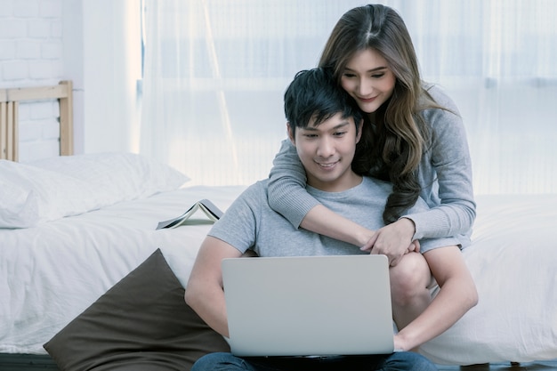 Closeup feliz amante asiática ou casal conversando e sorrindo ao usar o laptop de tecnologia na cama em b