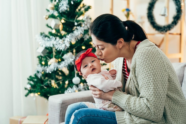 closeup fêmea asiática inclinando-se para seu lindo bebê, vai beijá-la. feliz nova mãe segurando um bebê e franzindo os lábios de uma forma divertida.