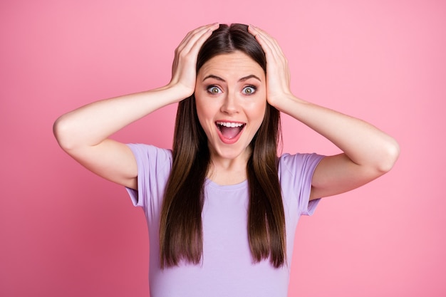 Closeup foto de atraente engraçado chocado senhora de bom humor penteado comprido boca aberta ouvir boas notícias braços na cabeça usar camiseta violeta casual isolado fundo rosa cor pastel