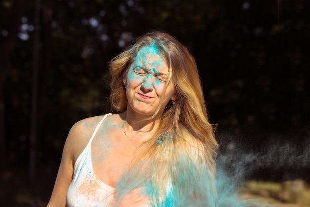 Closeup foto de expresiva mujer rubia con pelo largo y rizado celebrando el festival de Holi