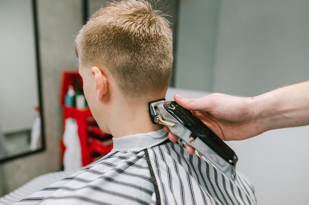 Closeup Foto Friseur Hand mit Clipper schneidet Haare des jungen Mannes