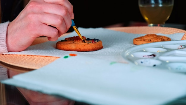 Closeup foto de manos de mujer pintando pan de jengibre en la cocina mujer decorando galletas