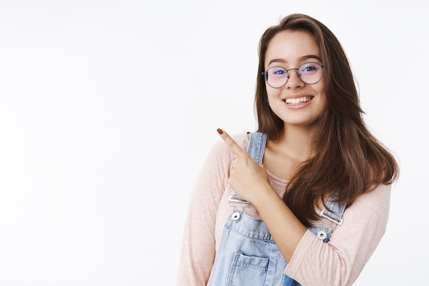 Closeup foto de mujer atractiva feliz entusiasta amistosa en vasos con cabello castaño apuntando a la parte superior izquierda