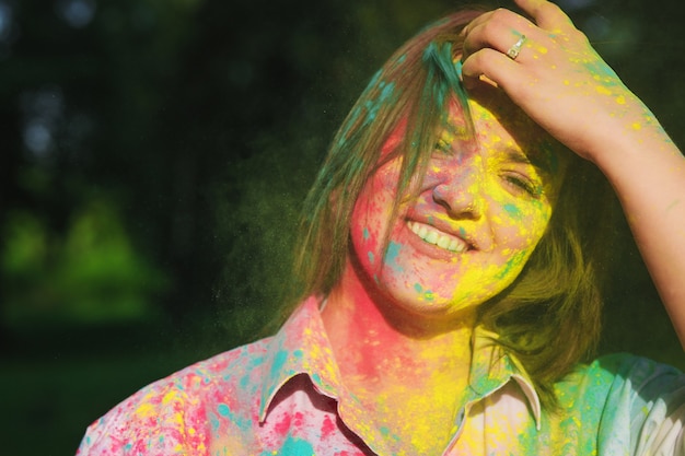 Closeup foto de mujer gloriosa con pelo corto cubierto de pintura amarilla Holi en el parque. Espacio para texto