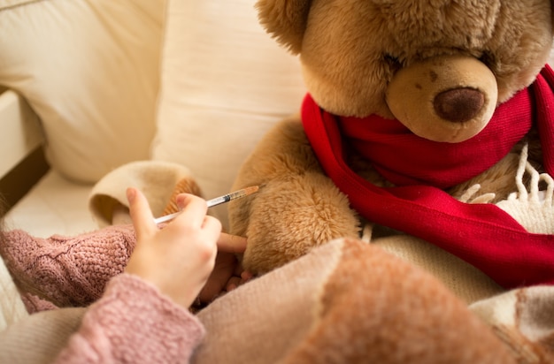 Closeup fotografia de uma menina a aplicar uma injecção a um ursinho de peluche doente